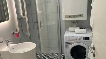 Ein kleines Badezimmer mit Dusche, Waschbecken und Waschmaschine.