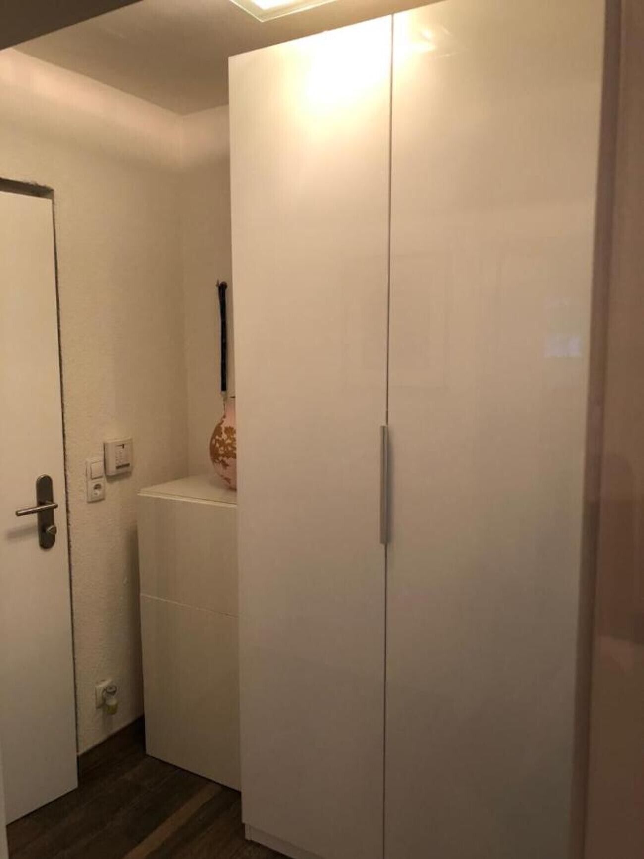 Une pièce avec une armoire, une porte et une petite étagère sur laquelle se trouve un vase.
