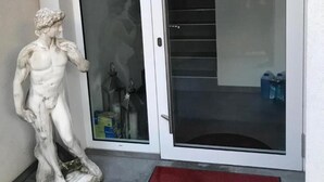 Une statue représentant une figure classique, une porte coulissante en verre et un tapis rouge à l’entrée.