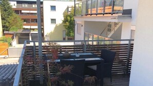 Un balcon avec une table et des chaises, des plantes en pot et une vue sur les bâtiments voisins.