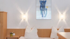 Una habitación de hotel con cama, dos lámparas de pared, un cuadro abstracto enmarcado y una mesita de noche con un florero.