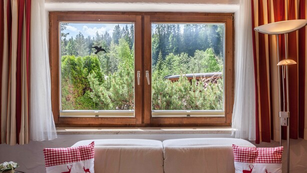 Una habitación con un ventanal grande, un sofá con cojines a cuadros y una lámpara.