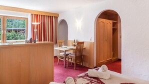 Una habitación con cama, una mesa de comedor con sillas, una ventana con cortinas, un armario de madera y una alfombra roja.