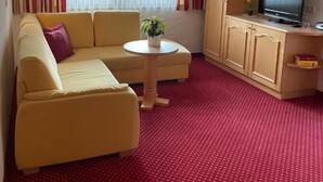 A hotel room with a yellow sofa, a small round table with a plant, a TV on a wooden cabinet, and a red carpet. - Apartment W2 Haus Ganghofer with Mountain View, Shared Terrace & Wi-Fi (Leutasch)