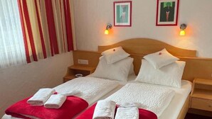 A double bed with white linens and red towels, two bedside tables with lamps, and two framed pictures on the wall. - Apartment W2 Haus Ganghofer with Mountain View, Shared Terrace & Wi-Fi (Leutasch)