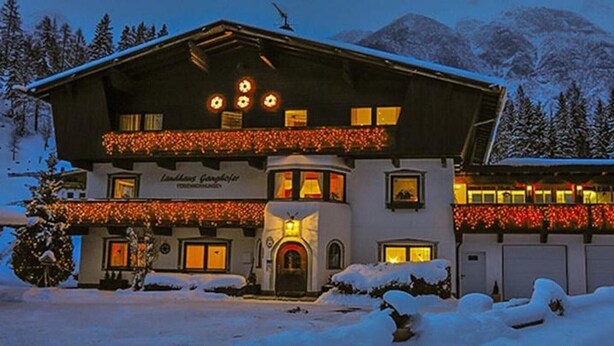 Un bâtiment à deux étages, avec un paysage enneigé, une montagne en arrière-plan et des fenêtres illuminées.