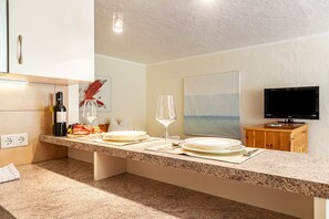 A modern kitchen with granite countertops, a wine bottle, a glass, and a painting on the wall.
