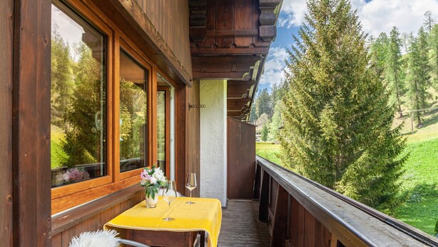 Een houten balkon met een tafel en stoelen, met uitzicht op een bebost gebied.