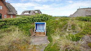 A beach chair in a natural setting with a path leading to it, surrounded by greenery and houses in the background. - Holiday Apartment 'Haus Lazy Dolphin No. 10' with Sea View and Wi-Fi (Rantum)