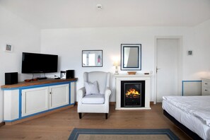 Un dormitorio con televisión, chimenea, sillón a rayas y cama.