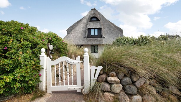 A thatched-roof house with a white gate, surrounded by greenery and rocks. - Holiday Apartment 'Haus Lazy Dolphin No. 10' with Sea View and Wi-Fi (Rantum)