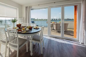 A dining area with a table set for breakfast, a view of the water, and a balcony with wicker furniture.