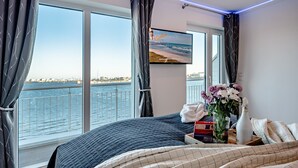 Un dormitorio con un ventanal grande, una cama, un televisor y un florero con flores.