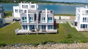 Una casa moderna de varios pisos con balcón, vista al agua y un camino de piedra que lleva a la entrada.