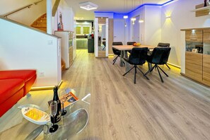 En moderne stue med spiseplads, en rød sofa og et køkken i baggrunden.