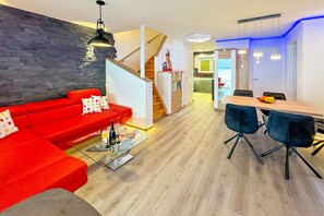 En moderne stue med en rød sofa, et glasbord og et spiseområde med et træbord og blå stole.