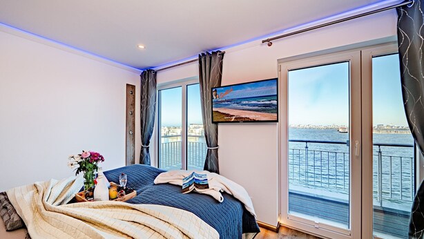 Un dormitorio con una cama, una ventana con vista al agua y un cuadro en la pared.