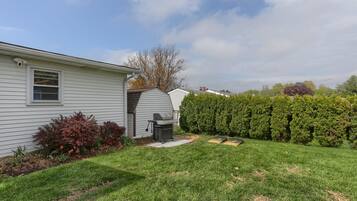 A residential backyard with a lawn, a barbecue grill, and a hedge.