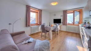 Ein modernes Wohnzimmer mit einer Couch, einem Esstisch mit Stühlen, einem Flachbildfernseher und einer Küchenzeile mit Schränken und einem Herd.
