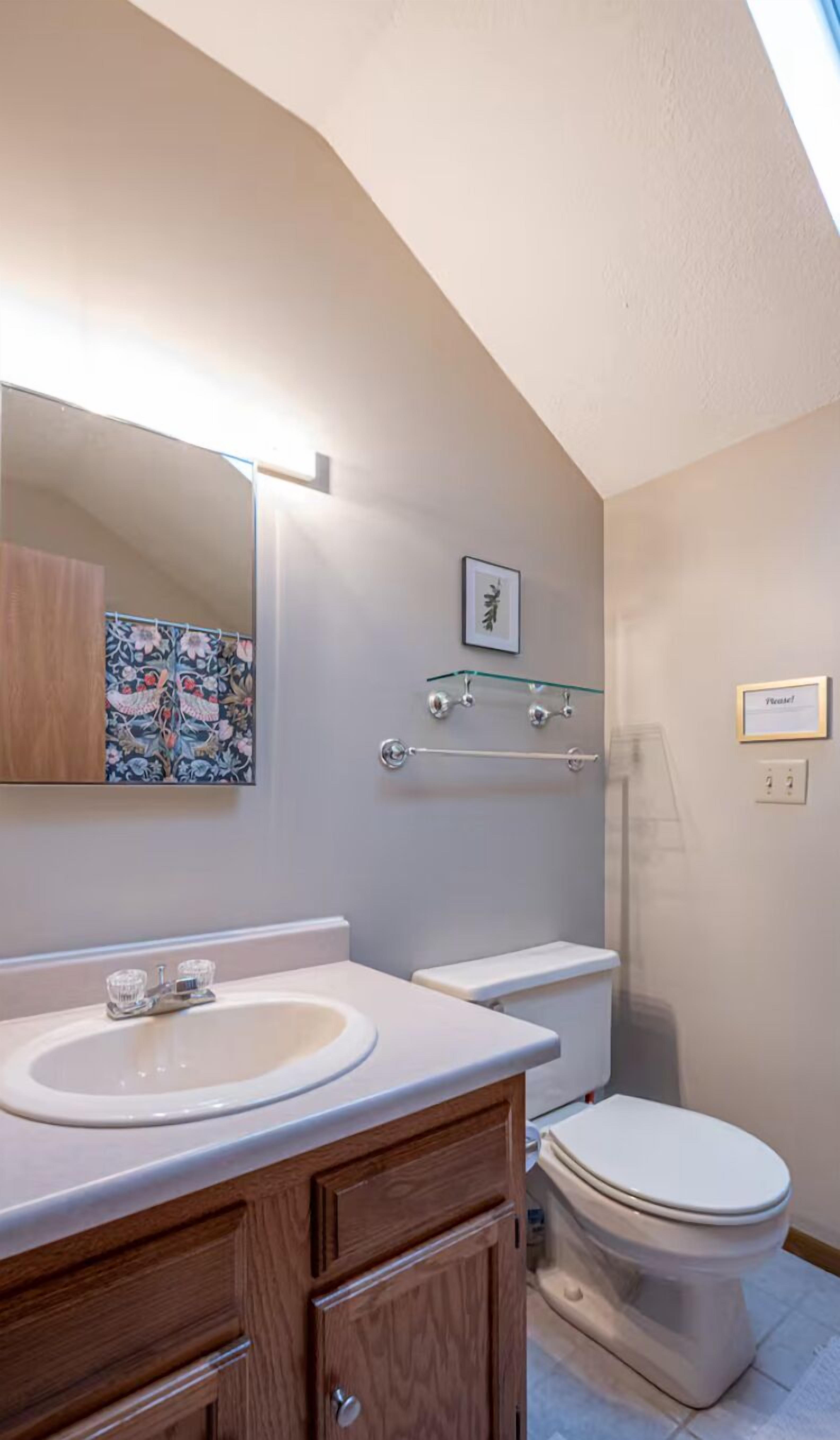 Un baño con tocador de madera, lavamanos blanco, inodoro y zona de ducha.