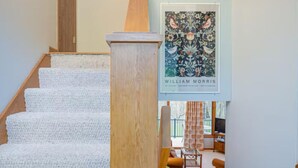 Eine Treppe mit Holzbalkonen und Teppichstufen führt in einen Wohnbereich mit Sofa und einem Gemälde.