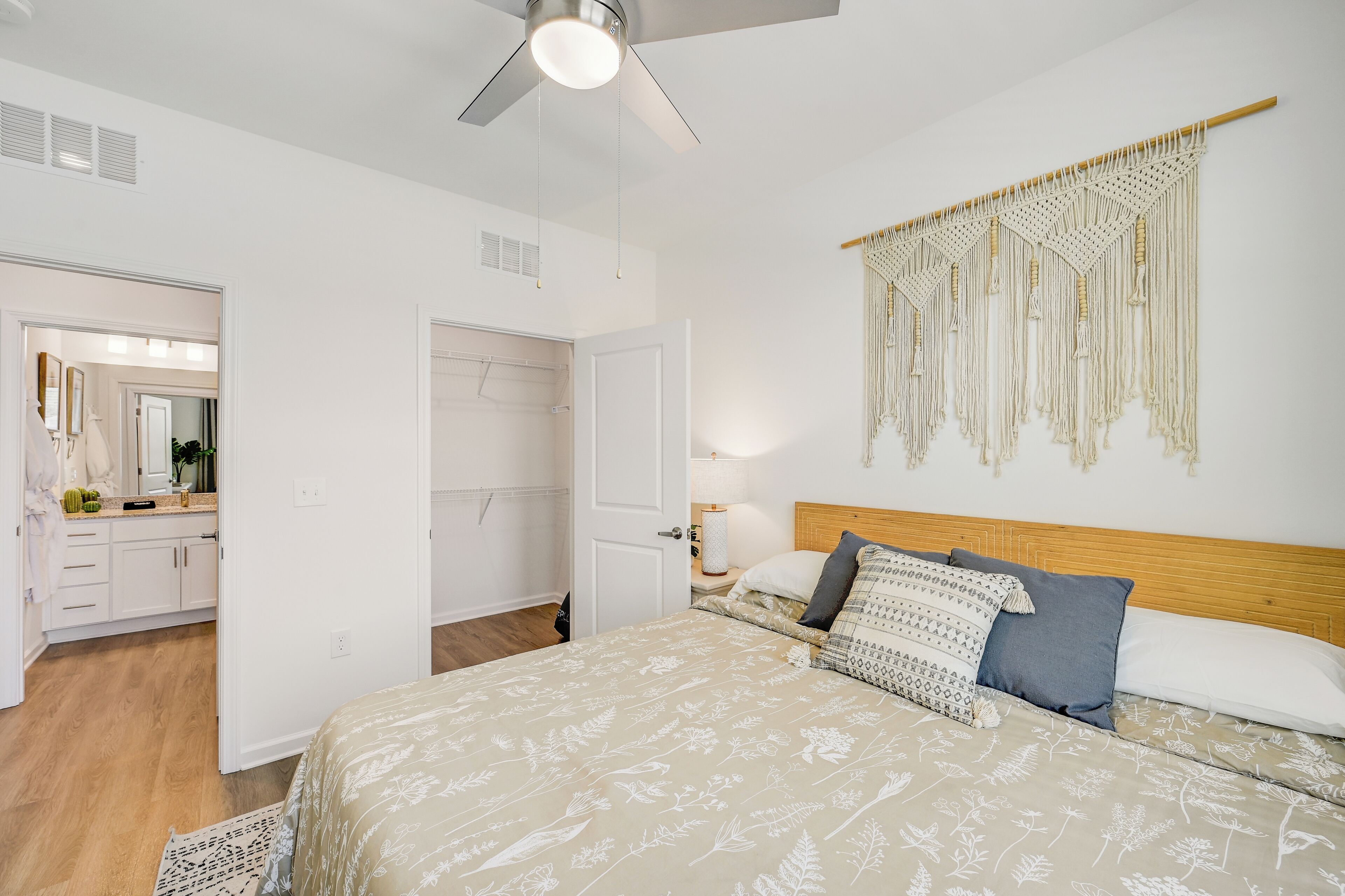 Una camera da letto con un letto, una ventola a soffitto, un arazzo macramè e una testiera in legno.
