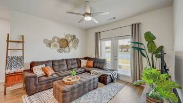 A modern living room with a sectional sofa, a ceiling fan, a decorative wall piece, and a large plant.