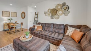 Un salon avec un canapé en cuir marron, une table à manger avec des chaises, et un mur décoré d’œuvres d’art circulaires tissées.