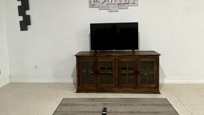 A living room with a wooden cabinet, a flat-screen TV, and a glass coffee table.