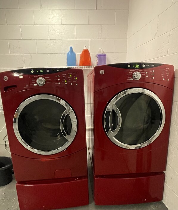 Twee rode wasmachines met een voorlaadklep in een wasserij met een witte bakstenen muur.