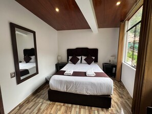 A modern bedroom with a large bed, a mirror, two bedside tables, and a window with a view of greenery. - SAYACMARCA CLASSIC INN (Machu Picchu)