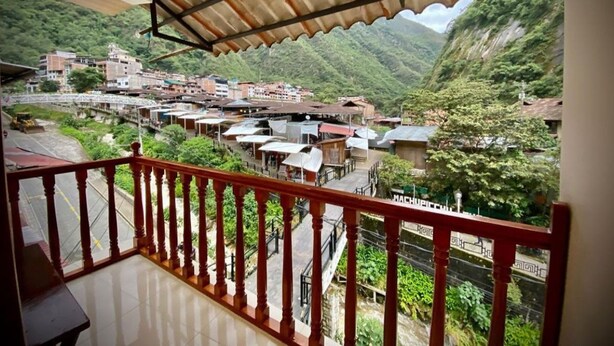 A balcony with a view of a hillside village, a metal roof, and a staircase. - SAYACMARCA CLASSIC INN (Machu Picchu)