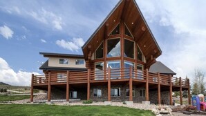 Une grande cabane en bois à plusieurs étages, dotée d’un balcon, située dans une zone herbeuse sous un ciel dégagé.