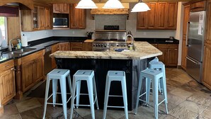 Une cuisine avec des meubles de rangement en bois, un îlot central doté de tabourets, une cuisinière et un réfrigérateur.