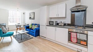 A modern kitchen with white cabinets, a stainless steel range hood, and a microwave. - Winkley House by Guestz (Preston)