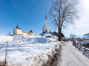 Sneeuwlandschap met boerderijen, een kerk, een klein gebouw en een houten hek langs een onverharde weg.
