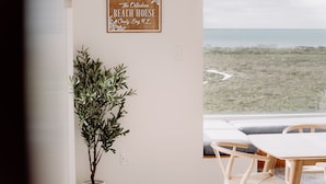 Een kamer met uitzicht op het strand, een potplant en een bordje met de tekst 'The Ostadian Beach House Cloudy Bay, NZ'.