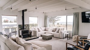 Een ruime woonkamer met een grote bank, een salontafel en een open haard. Grote ramen bieden uitzicht op het strand.