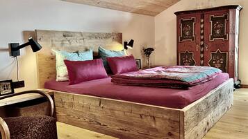 A bedroom with a wooden headboard, a bed with a red bedspread, two pillows, a nightstand with a lamp, and a wooden cabinet.