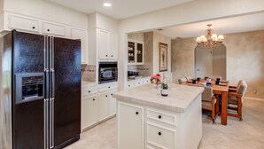A modern kitchen with white cabinetry, a black refrigerator, a built-in oven, and a dining area with a wooden table and chairs. - 🌵 Austin Escape with Private Pool, Ping Pong & Game Space | Roadrunner Retreat (Austin)