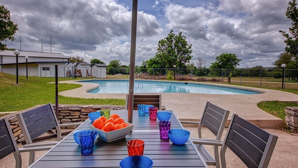 An outdoor pool area with a table set for dining, surrounded by chairs, and a covered seating area. - 🌵 Austin Escape with Private Pool, Ping Pong & Game Space | Roadrunner Retreat (Austin)
