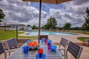 Un espace extérieur avec une piscine, une table dressée pour les repas, entourée de chaises, et un coin salon abrité.