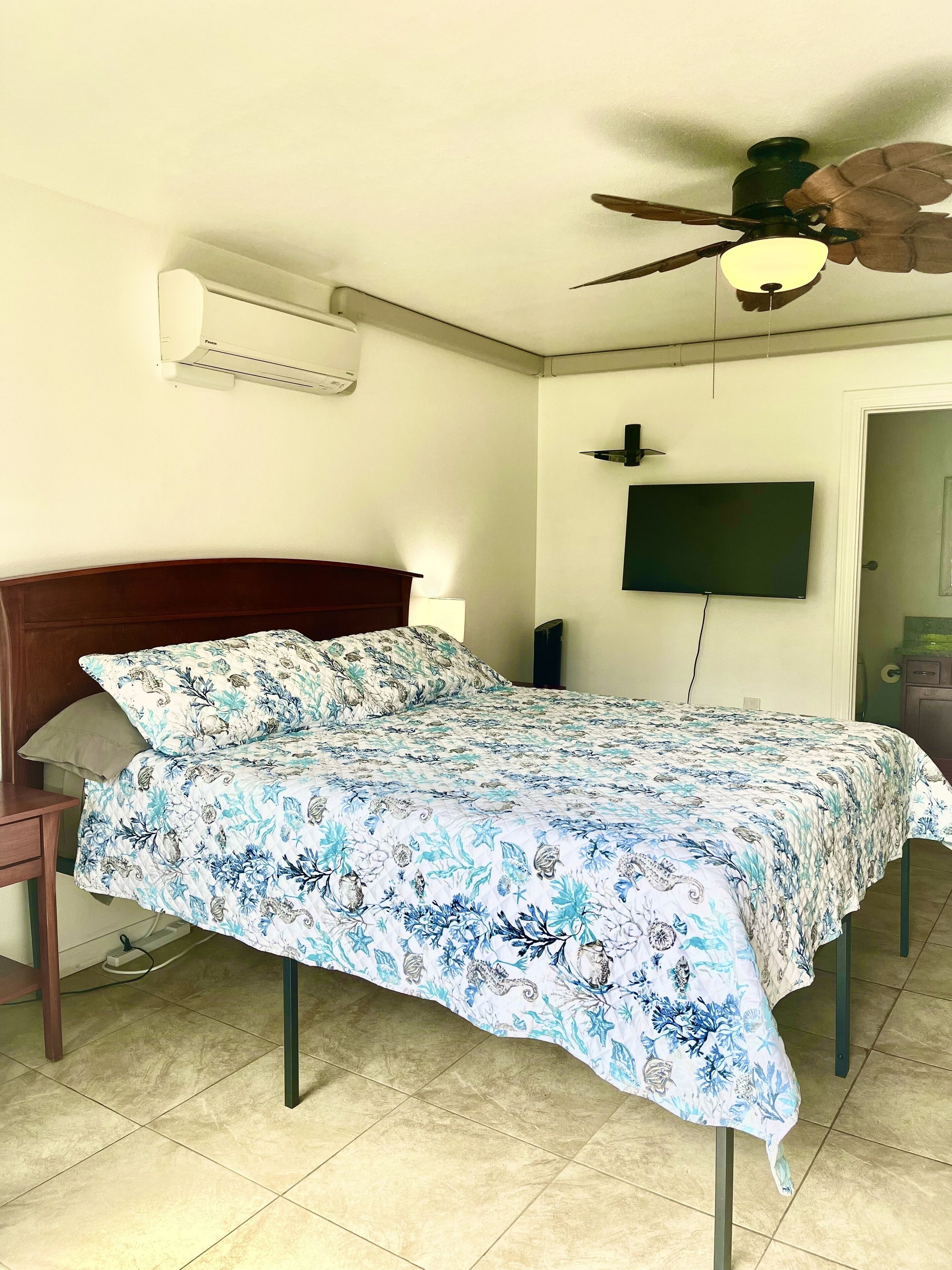 Une chambre à coucher comprenant un lit, un ventilateur de plafond, un téléviseur fixé au mur et un appareil de climatisation.
