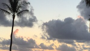 A sunset view from a balcony with a pool, palm trees, and a railing. - Cozy Studio By The Beach! 1BR (Kapaʻa)