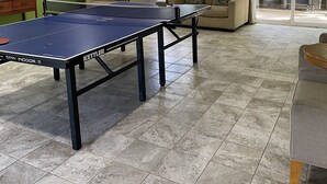 A spacious room with a ping pong table, a sofa, a television, and a window with blinds. - Cozy Studio By The Beach! 1BR (Kapaʻa)