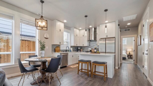 A modern kitchen with white cabinets, a central island with stools, and a dining area with a table and chairs.