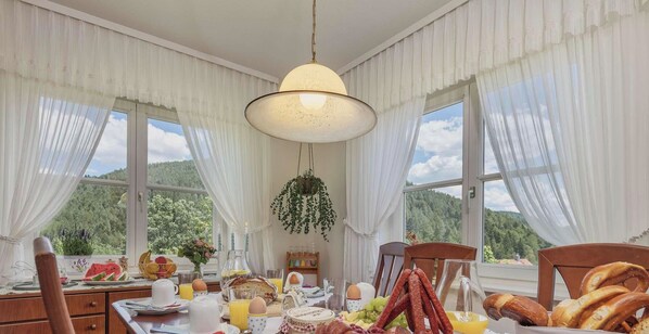 Un comedor con una mesa lista para el desayuno, una planta colgante y vistas al exterior.
