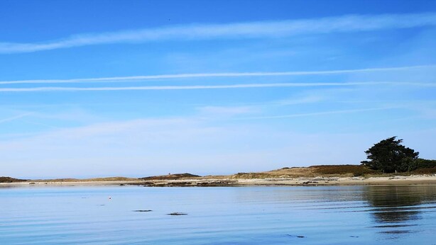 Un paysage côtier paisible avec un phare, une plage de sable et un ciel bleu dégagé.