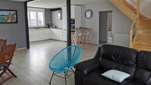 A modern living room with a black leather sofa and a blue chair, a wooden staircase, and a kitchen in the background. - Spacious house 200m from Lilia's beaches & restaurants (Plouguerneau)