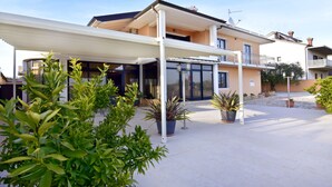 Una casa moderna de dos pisos con un porche cubierto, plantas en macetas y cielo despejado.